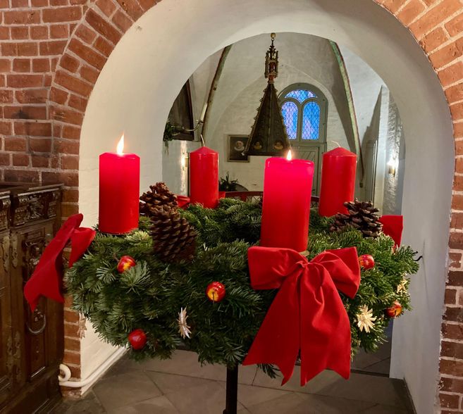 Adventskranz mit vier brennenden roten Kerzen in der St. Nicolai-Kirche Mölln unter einem gemauerten Bogen.