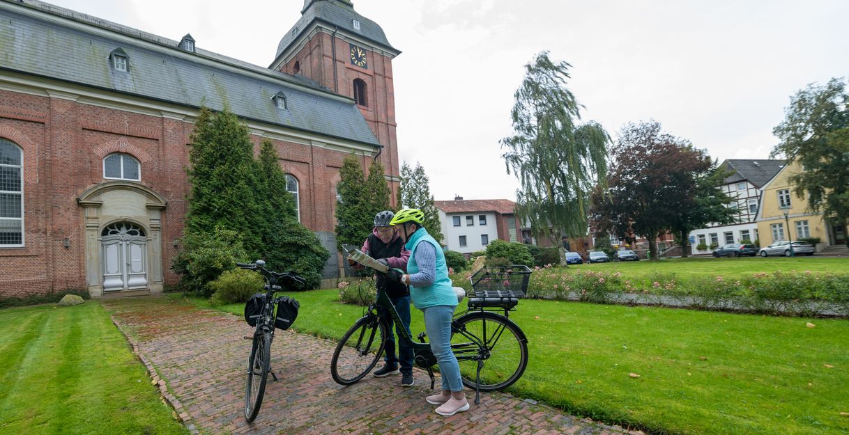 Zwei Personen mit Fahrrädern stehen vor einer Kirche und schauen auf eine Karte.