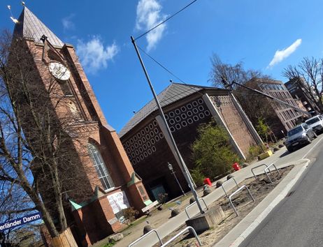 Kirche mit Turm und Uhr an einer Straße mit parkenden Autos.