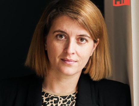 Porträt einer Frau mit schulterlangem Haar und einem schwarzen Blazer vor einem dunklen Hintergrund.