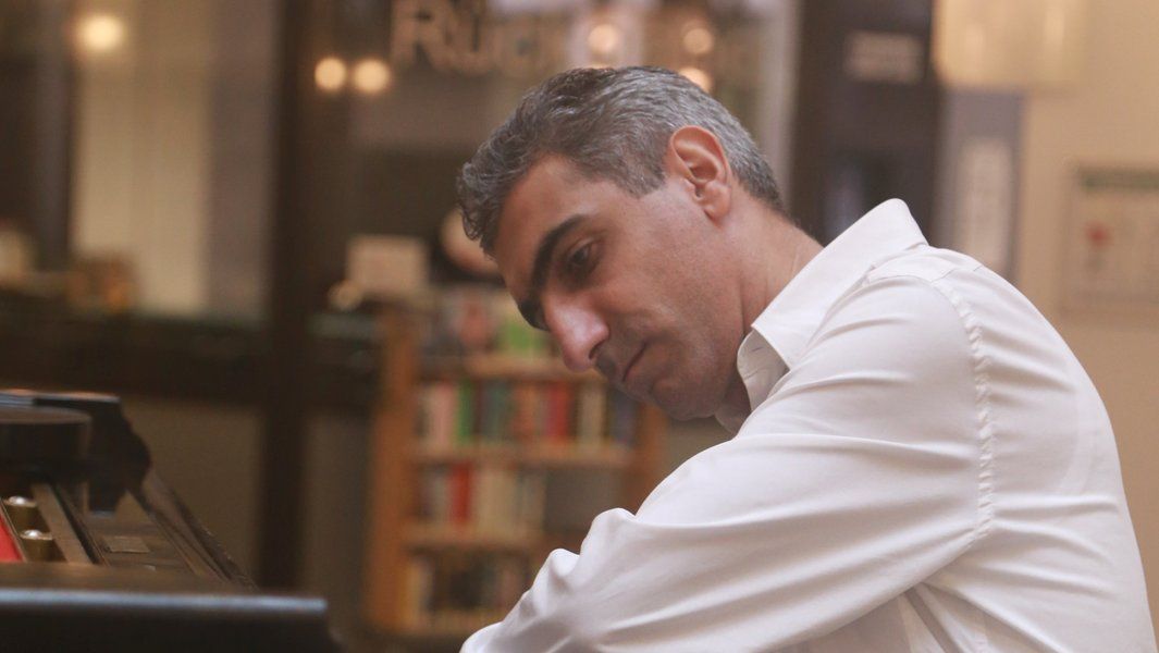 Ein Mann in einem weißen Hemd spielt konzentriert Klavier.