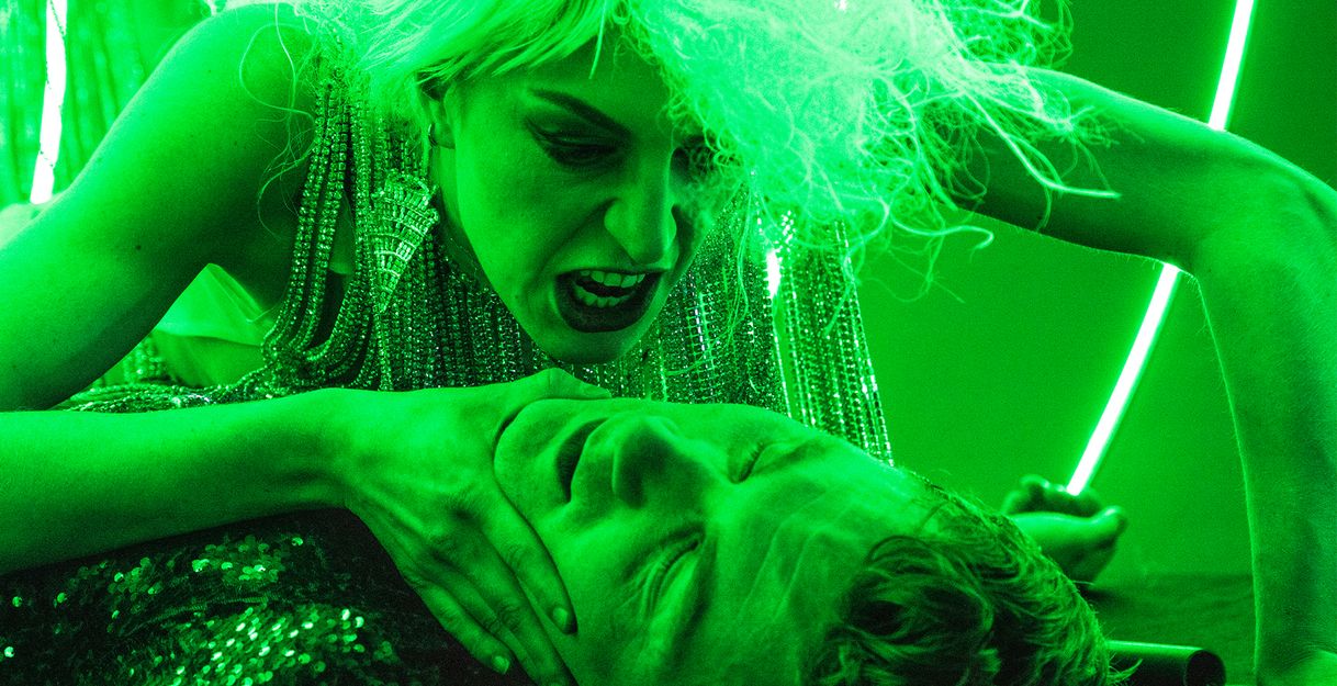Ein komplett in grünes Licht getauchtes Foto der Schauspielerin Alberta von Poelnitz, wie sie sich über den am Boden liegenden Schauspieler Paul Behren beugt und ihn am Kinn packt