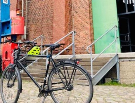Ein Fahrrad steht vor einem Backsteingebäude mit grüner Tür und Treppe.