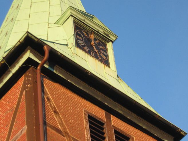 Nahaufnahme eines Kirchturms mit Uhr und grünem Dach vor blauem Himmel.