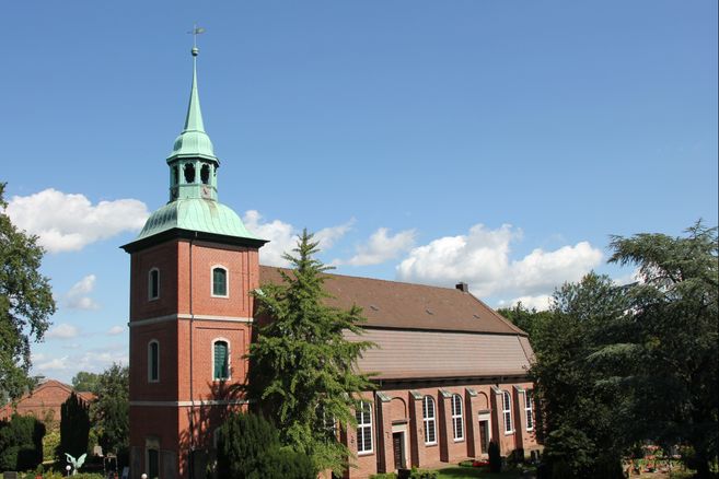 Kirche St. Pankratius in Ochsenwerder mit rotem Backstein und grünem Turm vor blauem Himmel.