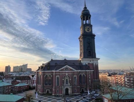Die St. Michaelis Kirche in Hamburg bei Sonnenuntergang, mit der Elbphilharmonie im Hintergrund.