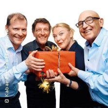 Vier Personen halten gemeinsam ein rotes Geschenk mit einer goldenen Schleife.