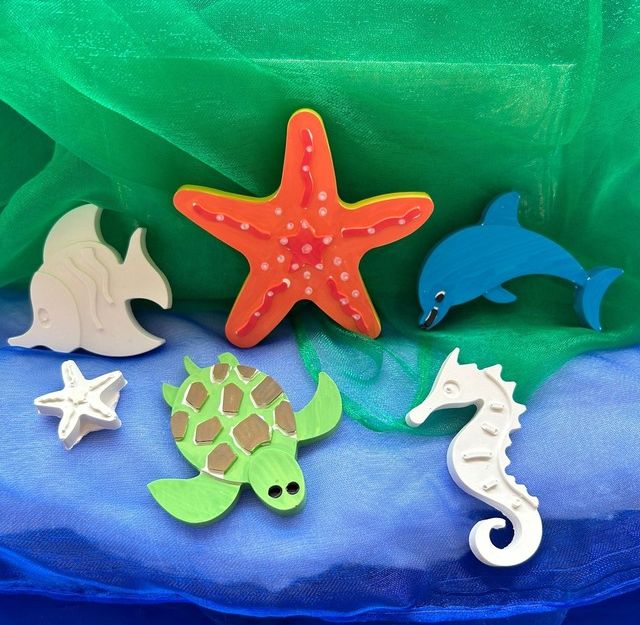 Bunte Gipsfiguren von Meerestieren auf blauem und grünem Stoff.