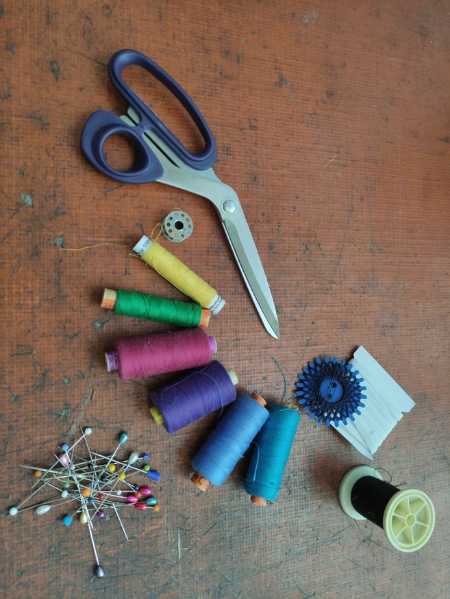 Schere, Garn in gelb,grün,pink,lila,blau und Türkis. Ein Haufen Stecknadeln.