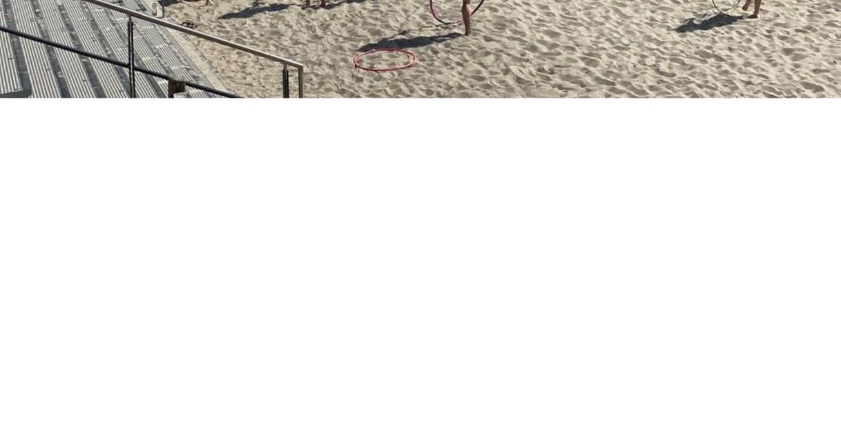 Gruppe von Menschen mit Hula-Hoop-Reifen am Strand vor einer Seebrücke.