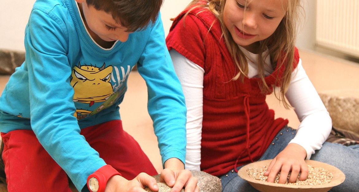 Zwei Kinder mahlen Getreide mit Steinen.