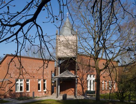 Backsteinkirche mit Glockenturm und Bäumen im Vordergrund.