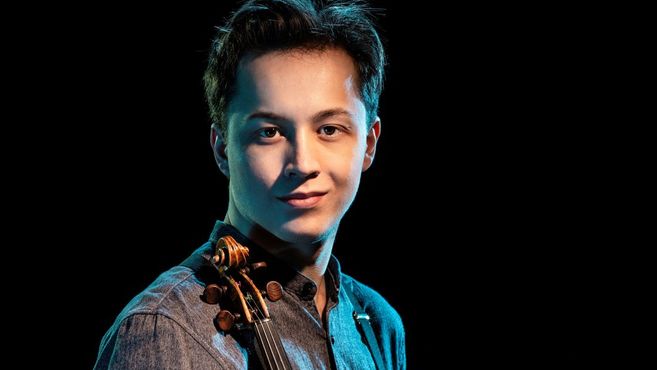 Ein junger Mann mit einer Geige vor einem dunklen Hintergrund.