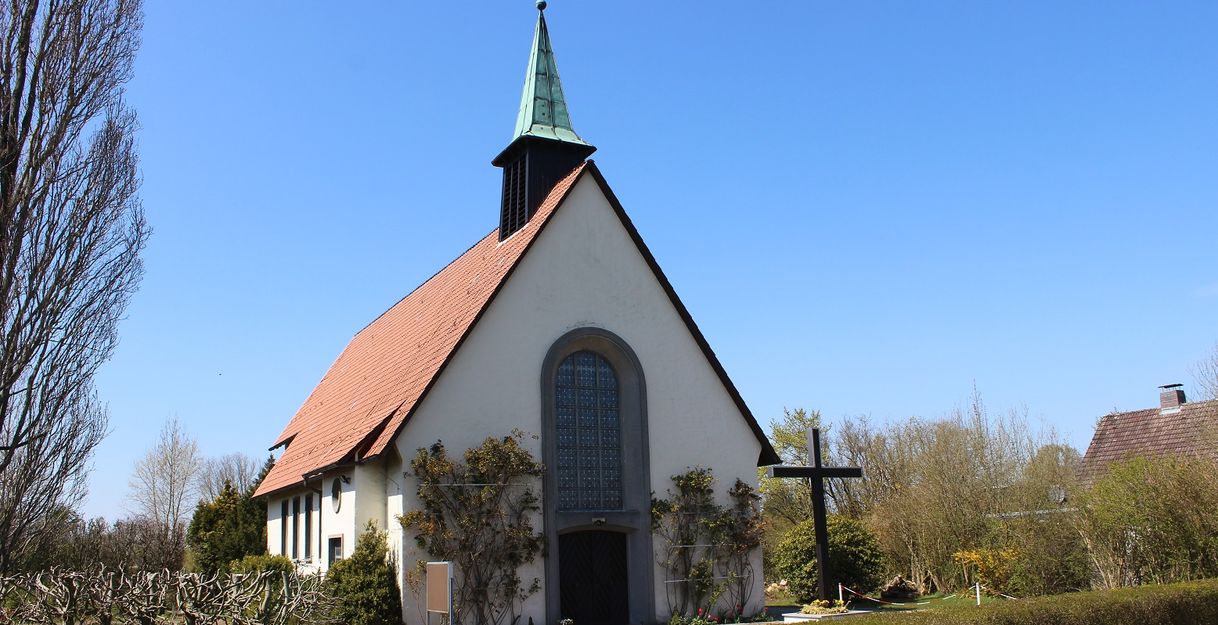 Eine kleine Kirche mit rotem Dach und grünem Turm vor blauem Himmel.