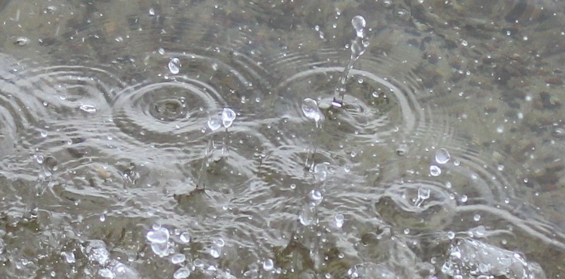 Nahaufnahme von Regentropfen, die auf eine Wasseroberfläche fallen und konzentrische Kreise bilden.