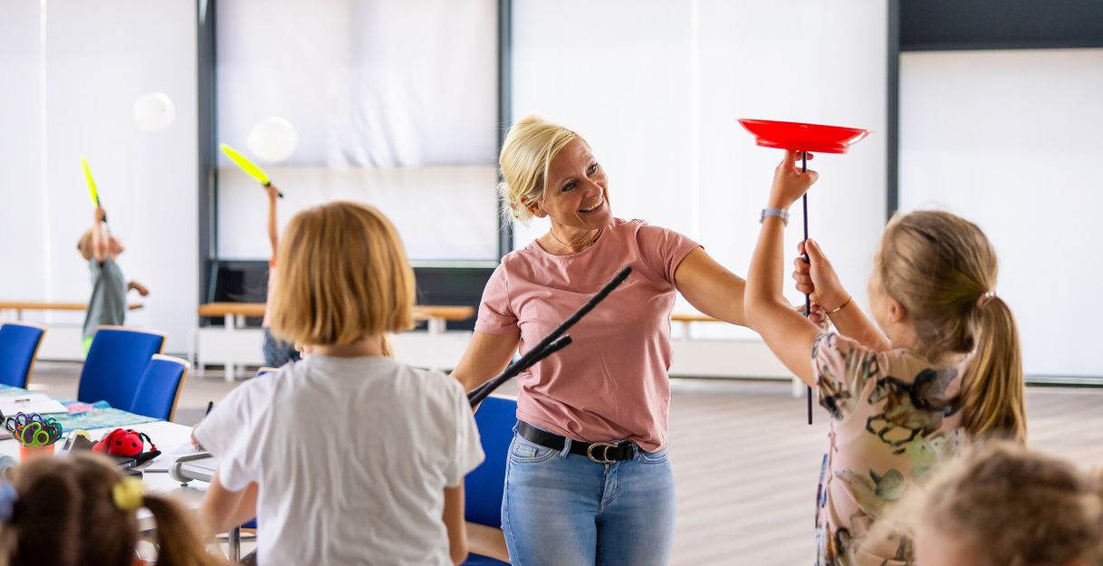 Eine Frau zeigt Kindern, wie man Teller auf Stöcken balanciert.