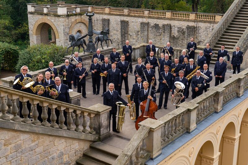 Das Landespolizeiorchester Brandenburg posiert in Uniformen auf einer Treppe vor einem historischen Gebäude.