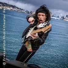 Gitarrist mit E-Gitarre vor Wasser und Stadt im Hintergrund.