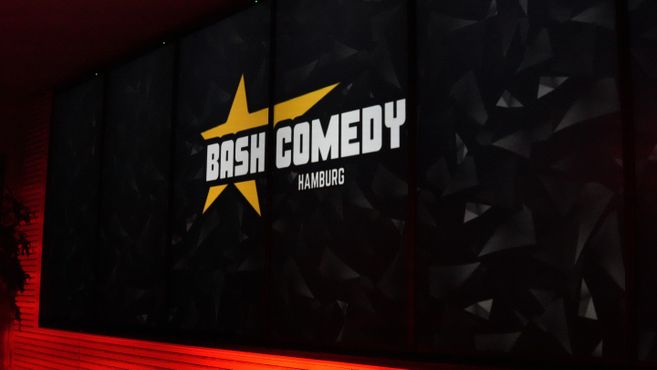 Ein Banner mit der Aufschrift 'Bash Comedy Hamburg' und einem gelben Stern auf schwarzem Hintergrund.
