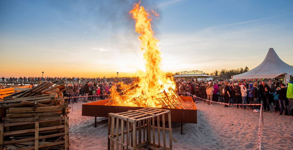 Osterfeuer am Strand von Pelzerhaken in der Lübecker Bucht bei Sonnenuntergang, umgeben von Menschen.