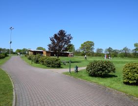 Golfplatz mit Übungsbereich und Personen beim Golfspielen unter blauem Himmel.