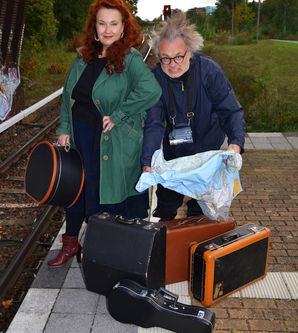 Zwei Personen stehen auf einem Bahnsteig mit mehreren Koffern und einer Karte.