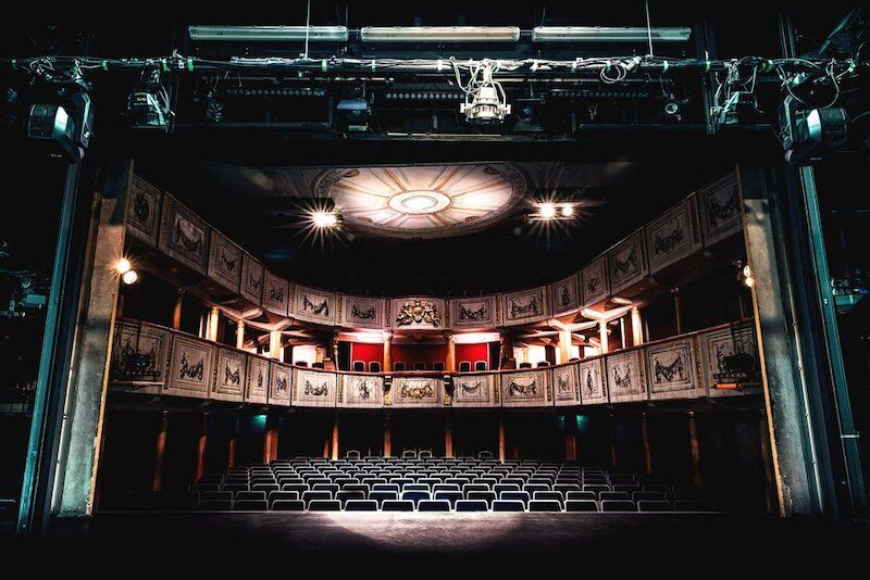 Innenansicht eines leeren Theatersaals mit dekorativen Balkonen und Deckenleuchter.