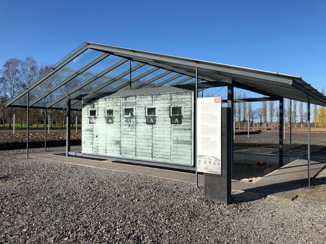 Ein offenes Metallgerüst in Form eines Hauses auf Schotterboden. Darin sind Darstellungen von der Außenwand des Arrestbunkers.