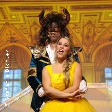 Zwei Personen in Kostümen auf einer Bühne, eine als Biest und die andere in einem gelben Kleid.