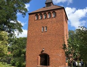 Backsteinturm mit Bäumen und blauem Himmel im Hintergrund.