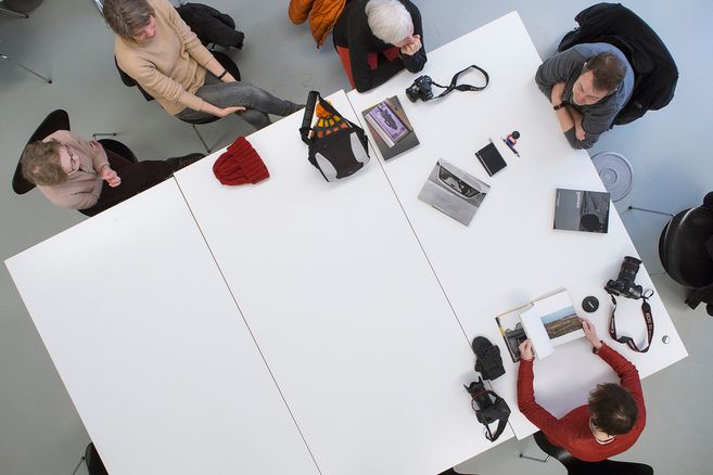 Menschen sitzen um einen großen Tisch mit Kameras und Fotobüchern.