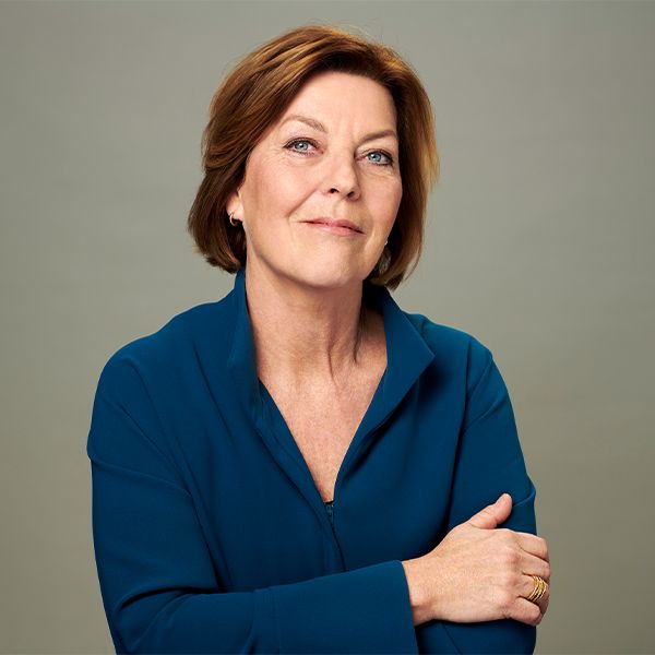 Porträt einer Frau in einem blauen Hemd vor grauem Hintergrund.