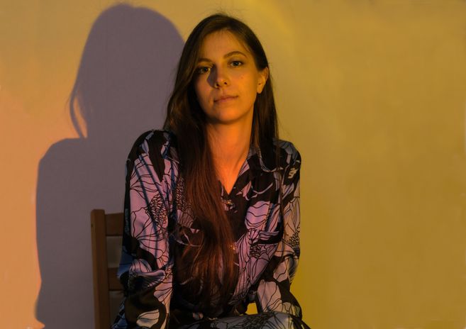 Eine Frau sitzt in einem Stuhl, beleuchtet von warmem Licht, das Schatten an die Wand wirft.
