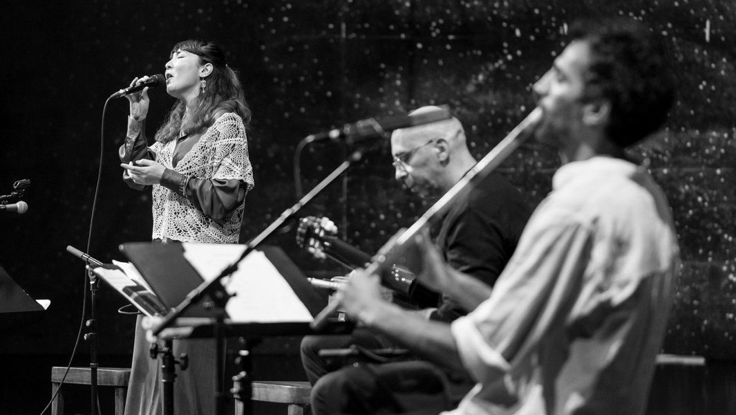 Schwarz-weiß-Foto einer Sängerin und zwei Musikern auf der Bühne.