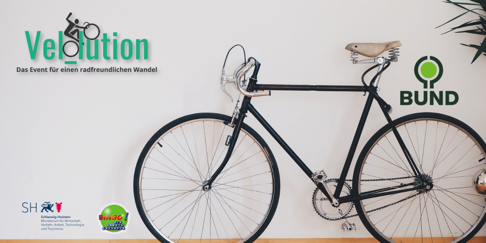Das Bild zeigt ein minimalistisches Design, in dem ein schwarzes Fahrrad an einer weißen Wand steht, der Boden ist aus Holz. Links oben ist das Logo der Veranstaltung "Velution" mit dem Slogan "Das Event für einen radfreundlichen Wandel". Rechts neben dem fahrrad ist das Logo des BUND (Bund für Umwelt und Naturschutz Deutschland) zu sehen. Unten links befinden sich die Logos der Bingo! Umweltlotterie und des Ministeriums für Wirtschaft, Verkehr, Arbeit, Technologie und Tourismus Schleswig-Holstein.