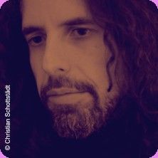 Porträt eines Mannes mit langen Haaren und Bart, der nachdenklich schaut.