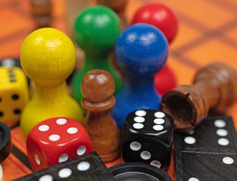 Nahaufnahme von bunten Spielfiguren, Würfeln und Dominosteinen auf einem Spielbrett.