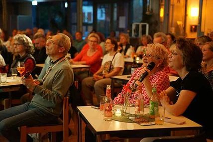 Menschen sitzen in einem gemütlichen Raum und singen Karaoke, während sie Getränke genießen.