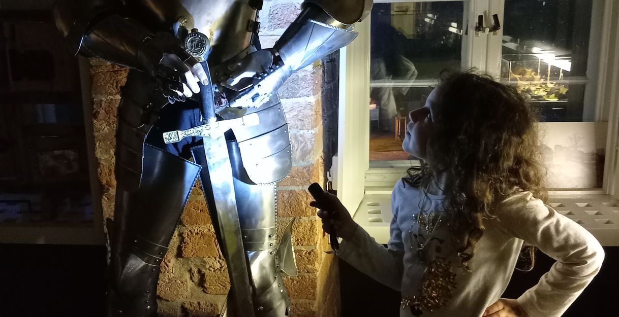 Ein Kind betrachtet eine Ritterrüstung in einem beleuchteten Raum mit Fenster im Hintergrund.