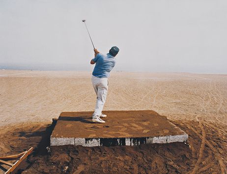 Ein Mann schlägt einen Golfball in einer Wüstenlandschaft.