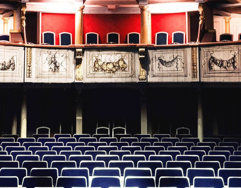 Innenansicht eines historischen Theaters mit blauen Sitzreihen und verzierten Balkonen.
