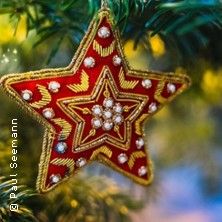 Ein roter, verzierter Weihnachtsstern hängt an einem Tannenbaum.