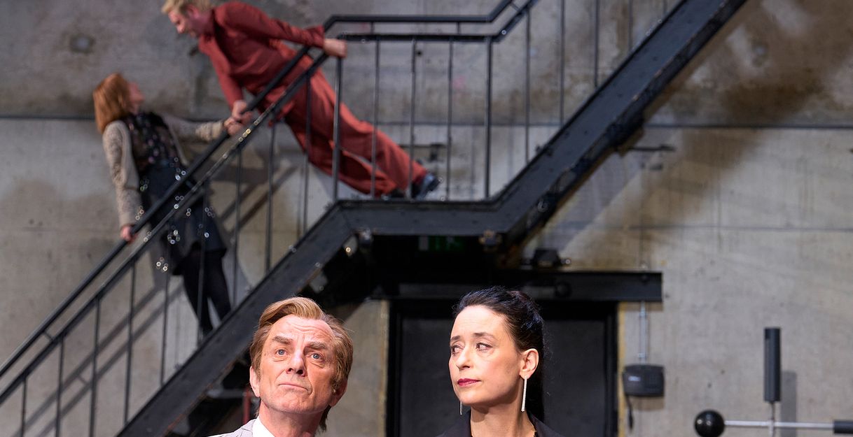 Im Vordergrund Magne Håvard Brekke und Sasha Rau, die ihn anschaut, er schaut geradeaus. Im Hintergrund Josefine Israel und Samuel Weiss auf einer schwarzen Metalltreppe. Josefine Israel hält sich mit beiden Händen am Geländer fest und lehnt sich leicht zurück, während sie nach oben zu Samuel Weiss schaut. Dieser hält sich ebenfalls mit beiden Händen fest und neigt sich mit geradem Körper zu ihr herunter.