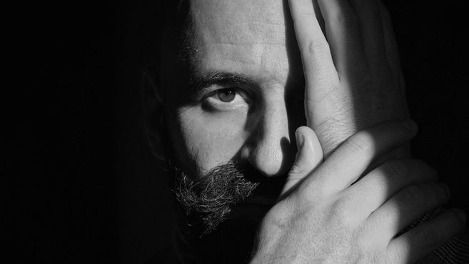 Schwarz-weiß Porträt eines Mannes, der sein Gesicht teilweise mit der Hand bedeckt.