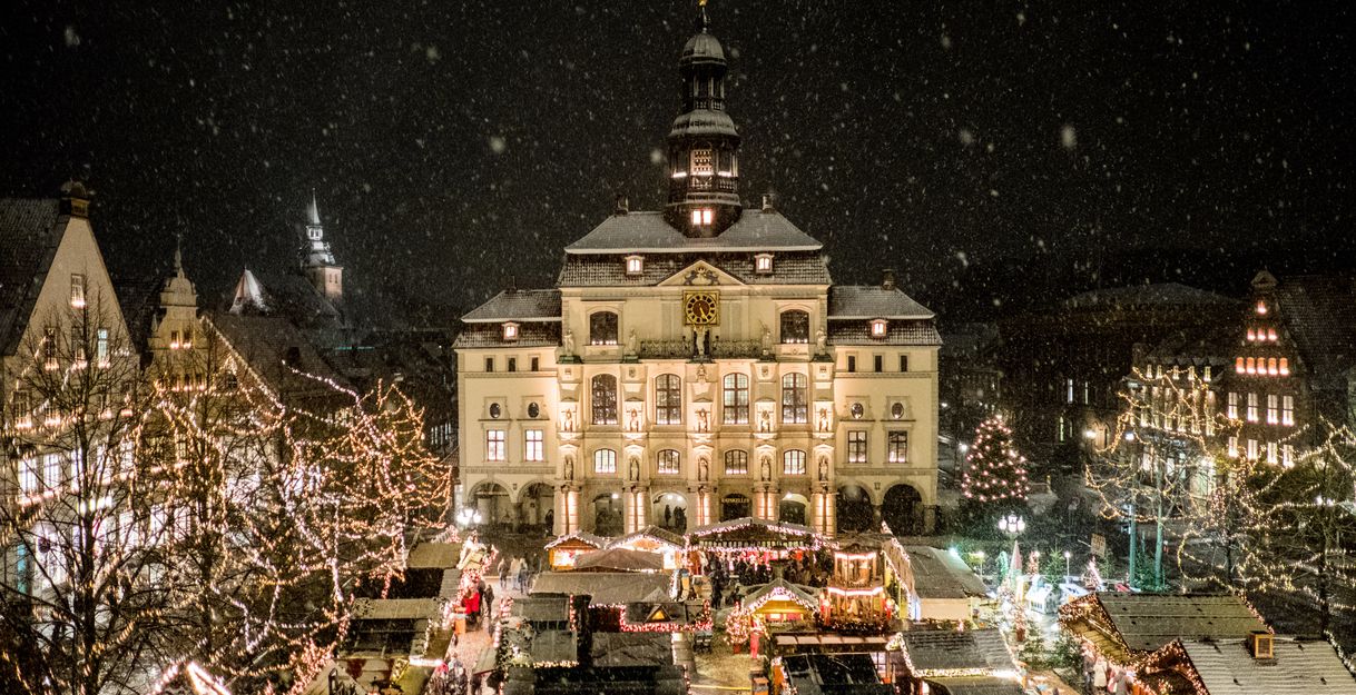 Weihnachtsmarkt in Lüneburg bei Nacht mit beleuchtetem Rathaus und schneebedeckten Ständen.