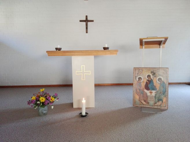 Ein schlichter Altar mit Kreuz, Kerzen, Blumen und einer Ikone in einem Kirchenraum.