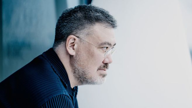 Ein Mann mit Brille und Bart schaut nach rechts. Er trägt ein dunkles Hemd und hat kurzes, graues Haar.