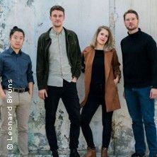 Vier Personen stehen vor einer verwitterten Wand und schauen in die Kamera.