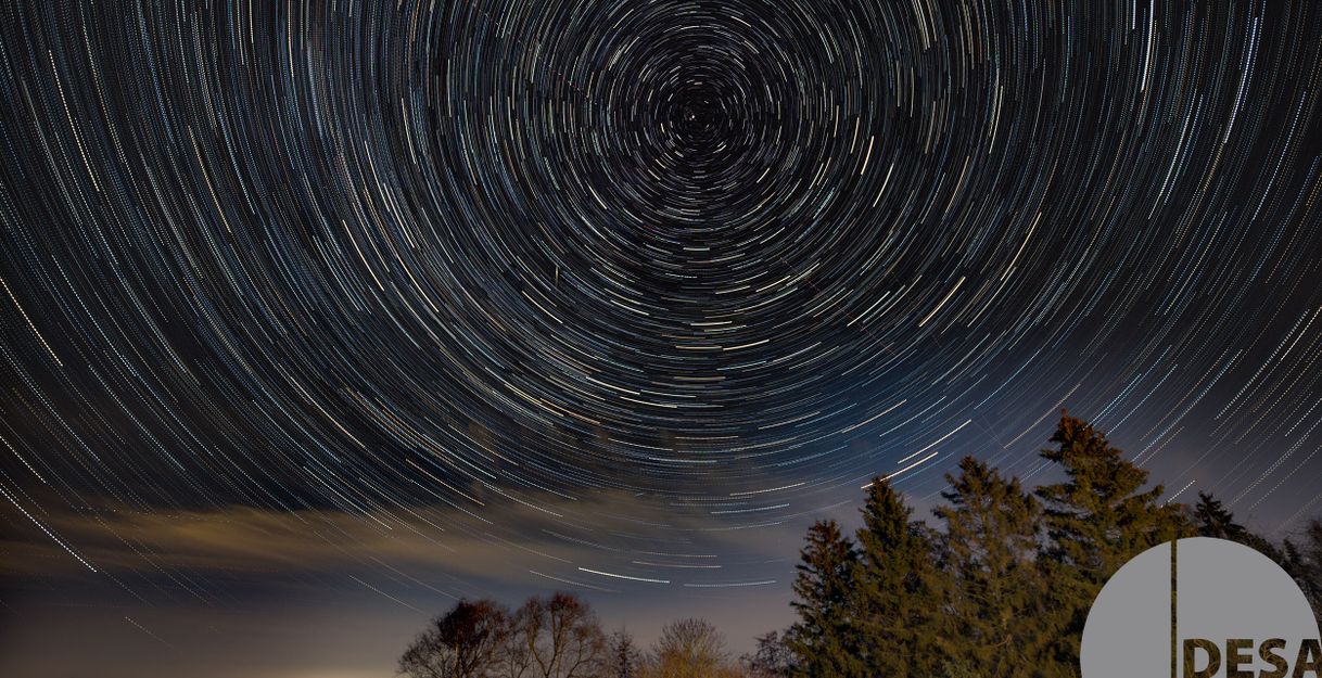 Langzeitbelichtung des Nachthimmels mit kreisförmigen Sternspuren über einem Wald.