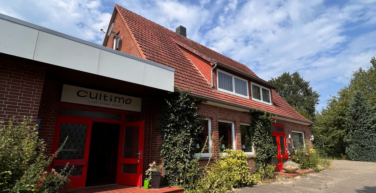 Außenansicht des Cultimo in Kuhstedtermoor mit rotem Eingang und Kletterpflanzen.
